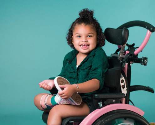 little girl with black curly hair in wheelchair in front of cyan background