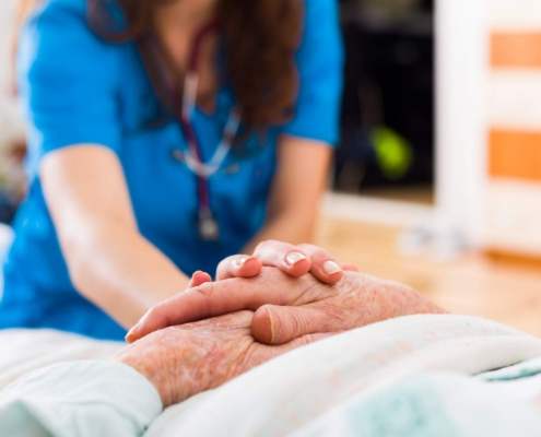 Nurse laying her hand on those of an eldery person in a bed