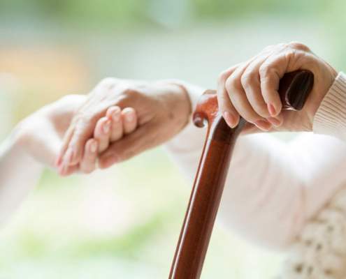 elderly woman with walking stick has her hand held by nurse